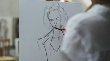 Eine Person skizziert eine Figur auf einer Leinwand.