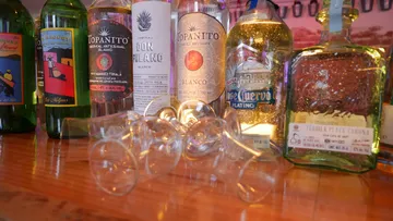 Bottles of tequila stand on a wooden table, glasses lie.