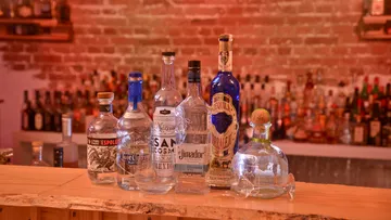 There are six tequila bottles on a wooden bar.