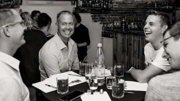 Five men laugh at the table in a bar.