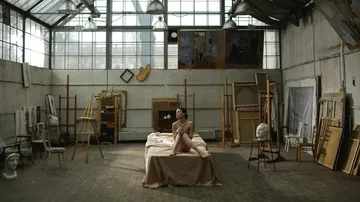 A naked person is sitting on a bed in a studio.