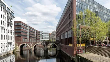 Two buildings, bridge over calm water, blue sky.