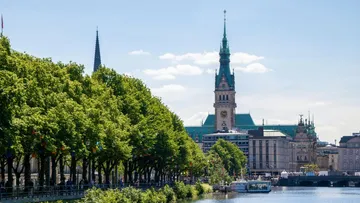 Grüne Bäume flankieren einen Fluss neben historischen Gebäuden.