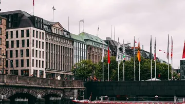 Modern buildings on a river surrounded by flags.