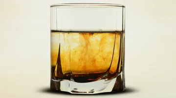 Ein Glas mit braunem Getränk steht vor hellem Hintergrund.