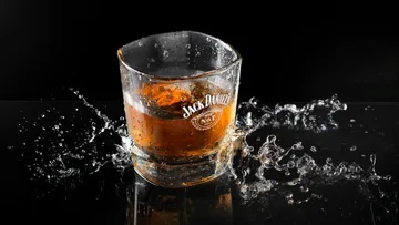 Ein Glas mit Whiskey spritzt Wasser auf schwarzem Hintergrund.