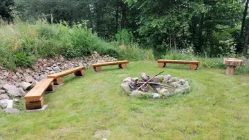 Wooden benches around a fire in a green meadow.