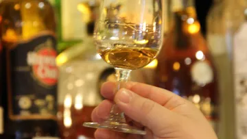 A glass of golden liquid is held, creative bar environment.