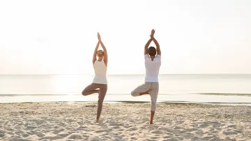 Zwei Personen praktizieren Yoga am Strand im Sonnenlicht.