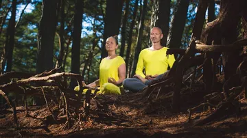 Zwei Menschen meditieren ruhig im Wald auf dem Boden.