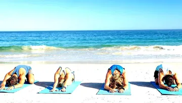 Four people are doing yoga on the beach under a blue sky.