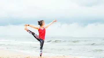 Woman in yoga area showing balance on the beach with clouds.