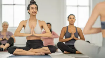 Frauen meditieren im Yoga-Sitz in heller Studioumgebung.