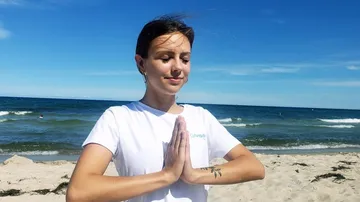 Young woman meditating on the beach under a blue sky.