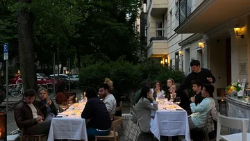 Tischgesellschaft isst und trinkt draußen in einer Stadtstraße.