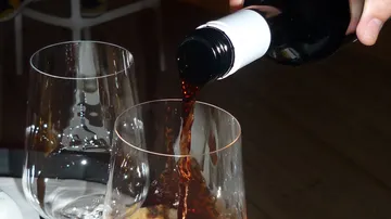 Eine Flasche gießt roten Wein in ein Glas.