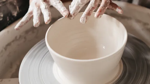 Hands form a clay bowl on a potter's wheel.
