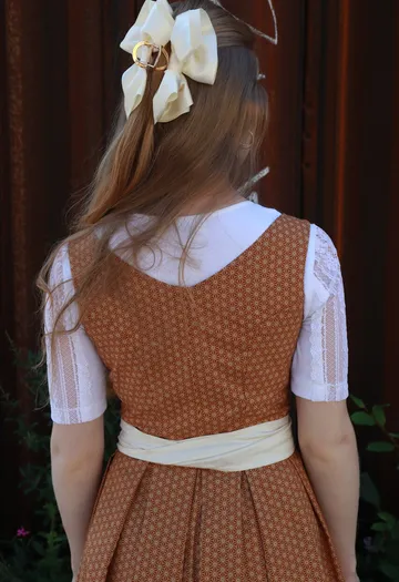 Ein Mädchen trägt ein braunes Kleid mit weißen Ärmeln.