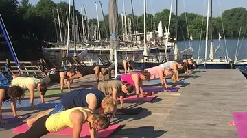 Group elements do yoga exercises on a jetty by the water.