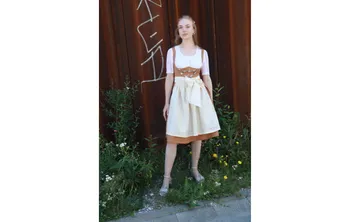 Frau in traditioneller Tracht steht vor einer rostigen Wand.