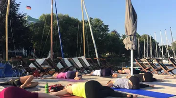 Yoga practitioners lie on mats by the water in the sun.