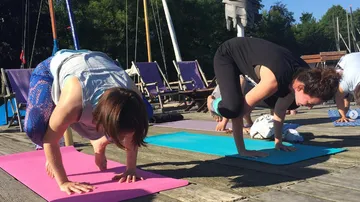 Zwei Frauen praktizieren Yoga auf Matten am Wasser.