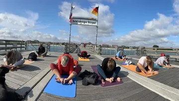 Gruppenvon Yogapraktizierenden dehnt sich am Strand.