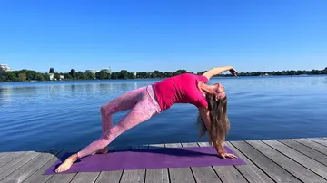 Frau übt Yoga am Ufer eines ruhigen Sees.