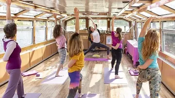 Frauen praktizieren Yoga auf einem Boot, umgeben von Wasser.