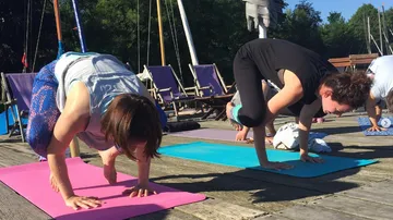Zwei Personen üben Yoga auf Matten am Ufer.