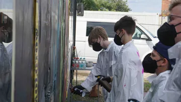 Menschen in Masken sprühen Wandgemälde im Freien.