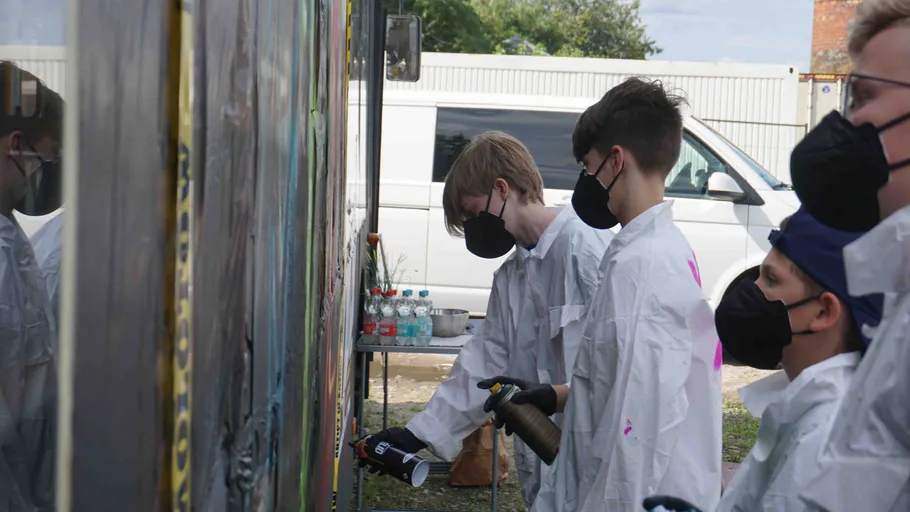 People in masks spray-painting outdoor mural.