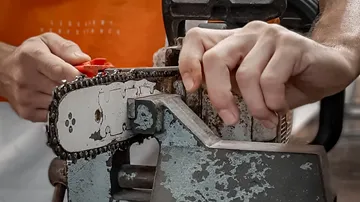 Hände schärfen eine Kettensäge in einer Werkstatt.