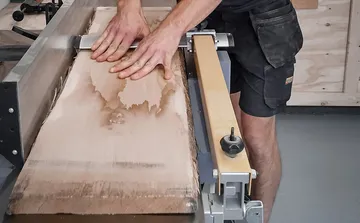Holz wird mit beiden Händen auf einer Maschinenoberfläche bearbeitet.