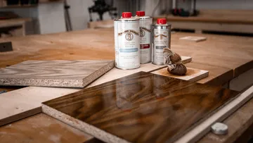 Holzplatten liegen auf der Werkbank, umgeben von Lackdosen.