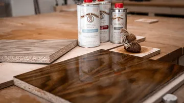 Holzplatten liegen auf einem Tisch, daneben Lackdosen stehen.