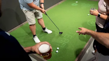 Mann puttet auf einem künstlichen Golfplatz, Freunde beobachten.
