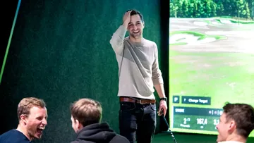 Laughing man with golf club playing in virtual golf game.