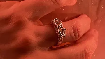 Silberner Ring auf einem Handfinger bei feuchtem Hintergrund.