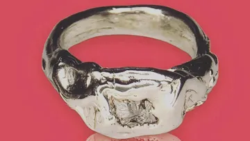 Silberner Ring mit unregelmäßiger Form vor rotem Hintergrund.