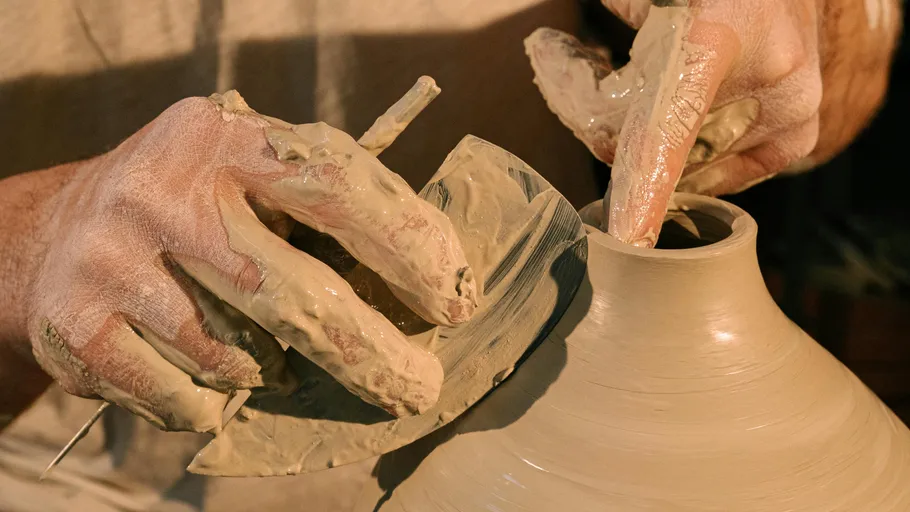 Potter's hands form a clay jug on a turntable.