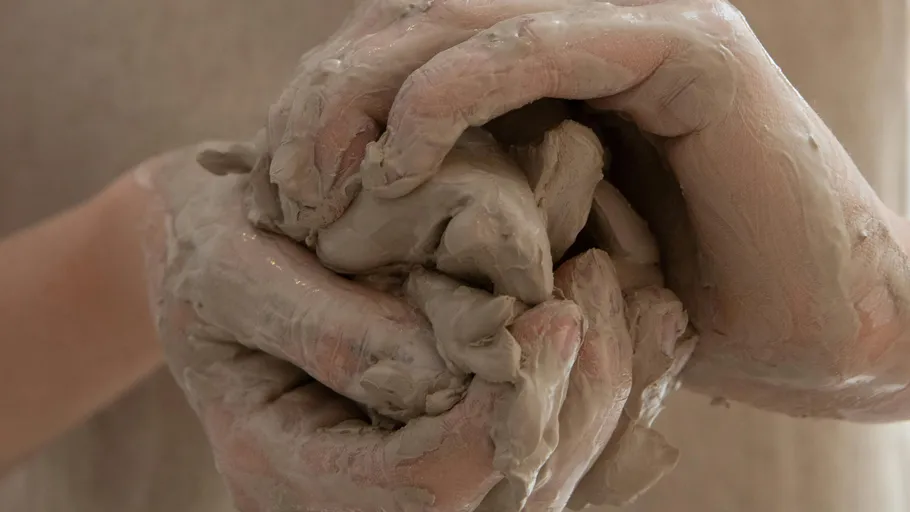 Hands form moist clay in a neutral space.