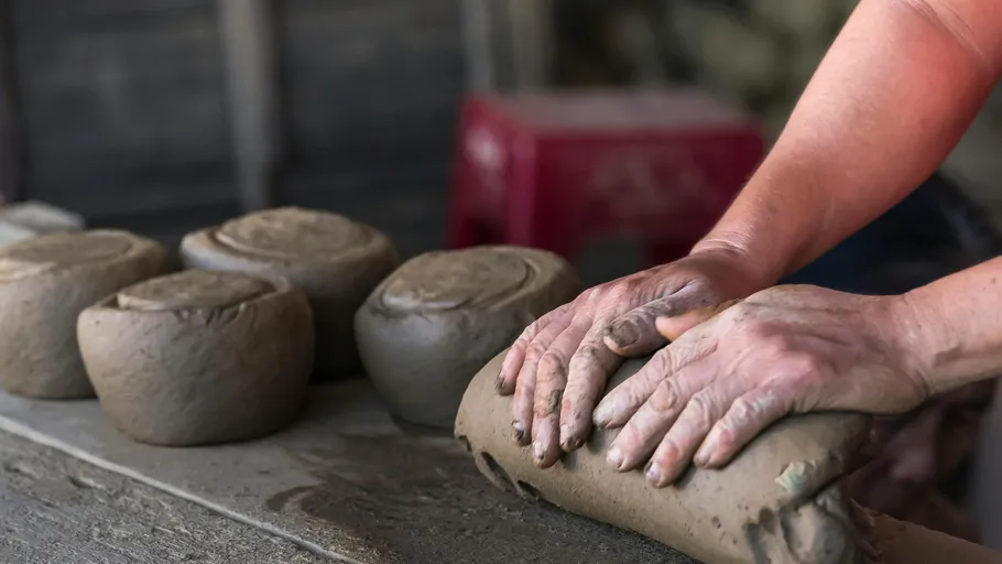 Pottery hands work on wet clay on a work surface.