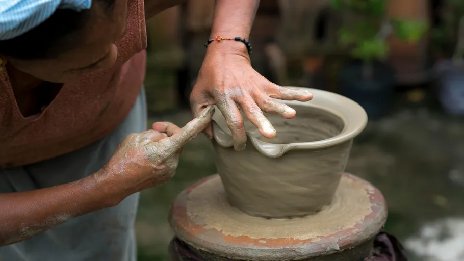 Potter sculpts clay pot with hands in a craft workshop.
