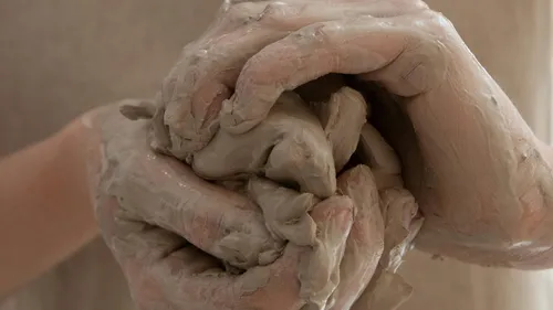 Hands form moist clay with close attention.