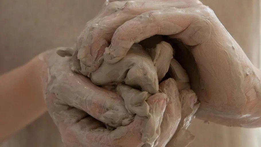 Hands form moist clay with close attention.