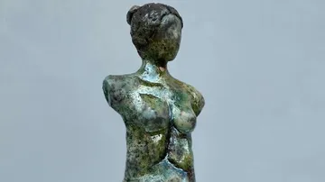 A small statue stands upright, its surface is shiny.