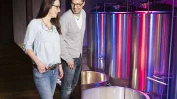 Two people look at shiny stainless steel containers in a room.