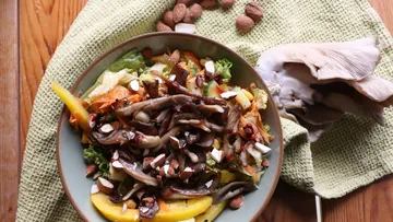Bunte Salatschüssel mit Pilzen und Nüssen auf Tisch.