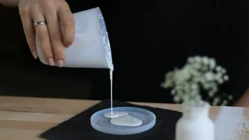 Eine Hand gießt cremige Substanz in eine Form.